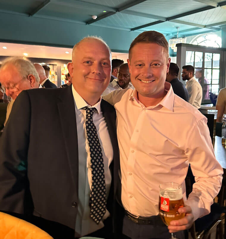 Two men having their picture taken in a bar holding drinks and smiling